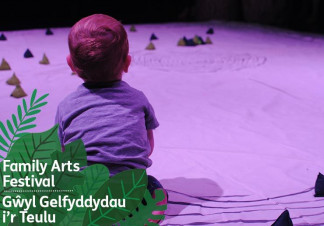 A toddler sits surrounded by artwork