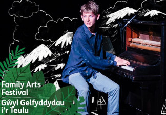 A boy sits and plays a piano in front of an illustrated background of mountains in black and white