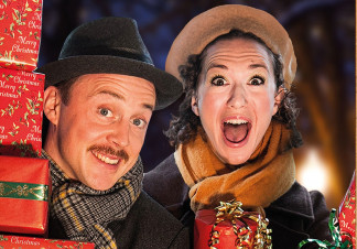 A man and woman stand in a doorway carrying a load of Christmas presents
