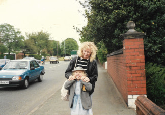 A mothers squeezes the cheeks of her daughter. They are standing on street pavement as cars drive by